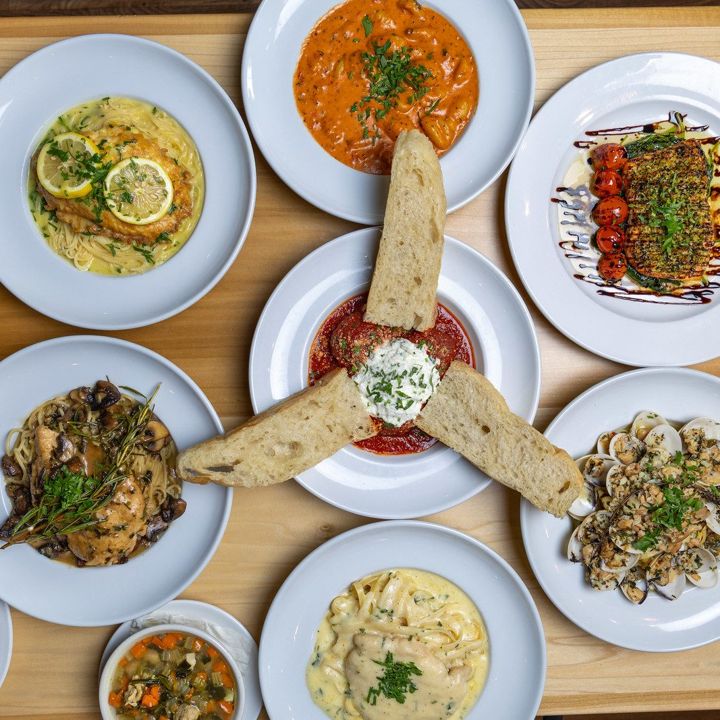 Overhead spread of pasta, seafood and flatbread dishes on a wood table