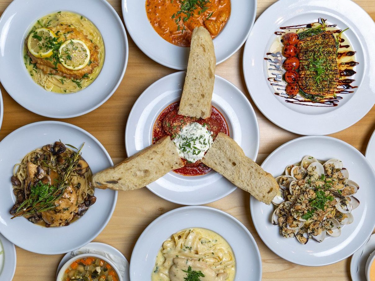Overhead spread of pasta, seafood and flatbread dishes on a wood table
